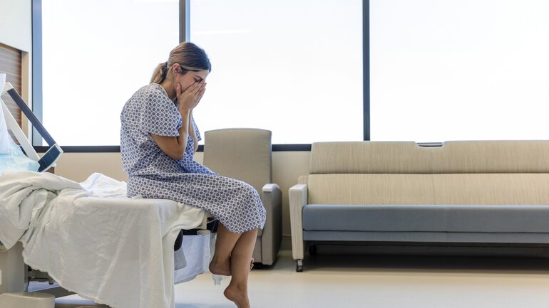 Traurig und nachdenklich sitzt eine Frau auf einem Bett im Krankenhaus.