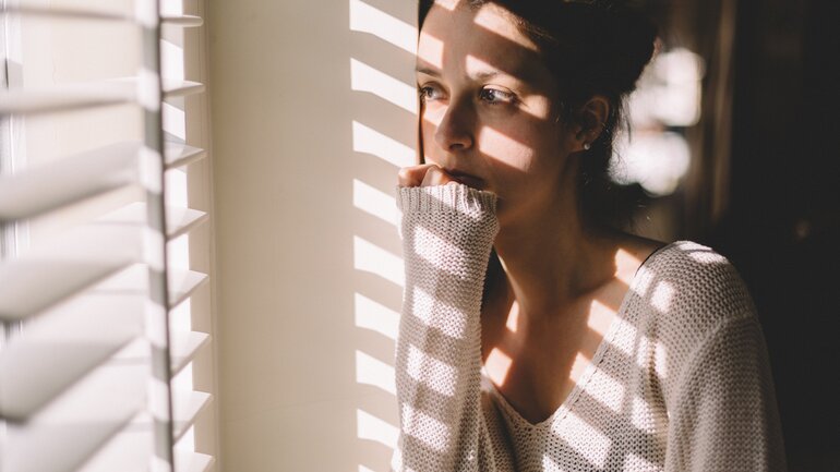 Frau steht traurig am Fenster