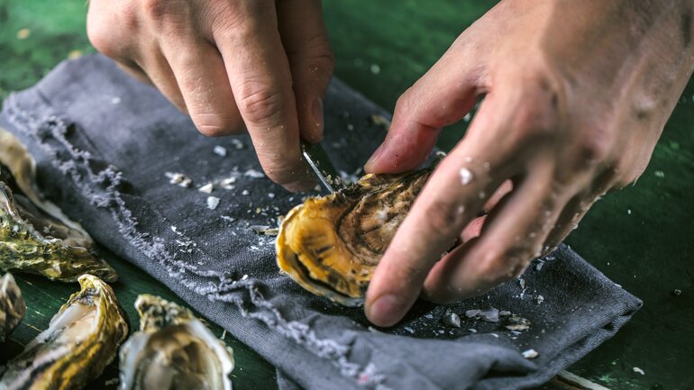Mann öffnet Austernschalen mit Messer