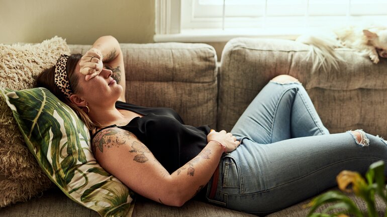 Frau liegt mit Schmerzen auf dem Sofa