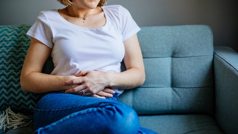 Frau sitzt auf dem Sofa und hat Magenschmerzen