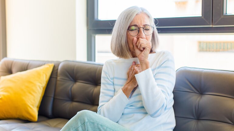 Frau sitzt hustend auf dem Sofa