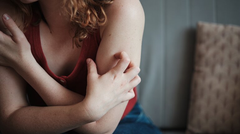 Nahaufnahme auf eine Frau mit roten Locken, sie sitzt auf einem Sofa und kratzt sich am Arm