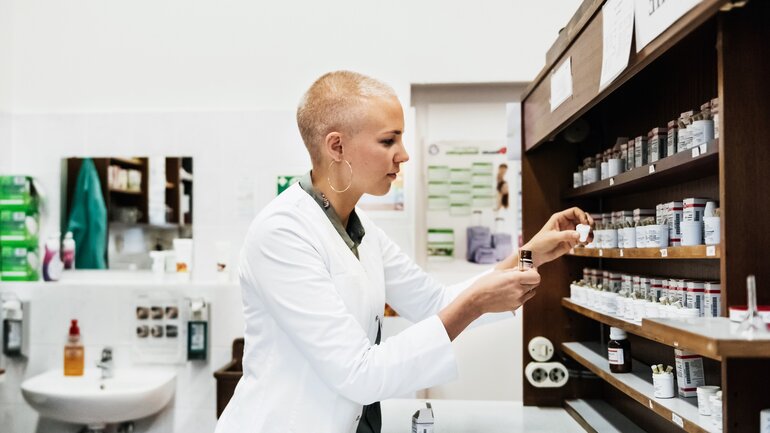 Junge Apothekerin sucht homöopathische Komplexmittel aus dem Regal