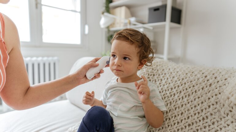 Mutter misst Fieber mit Thermometer im Ohr ihres kleinen Sohnes