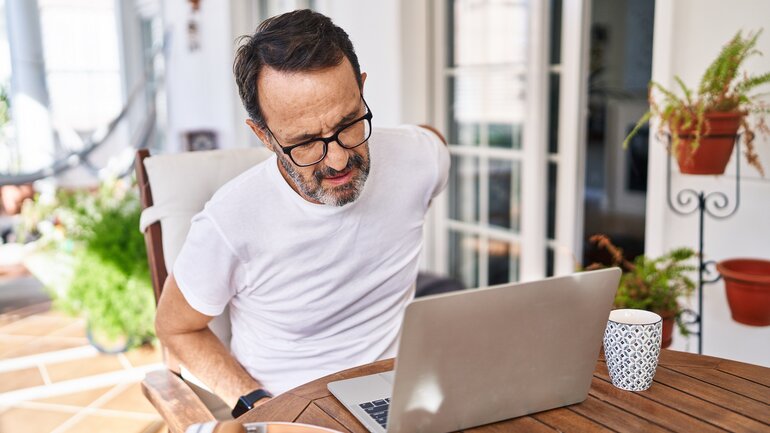 Mann im Homeoffice hat Rückenschmerzen