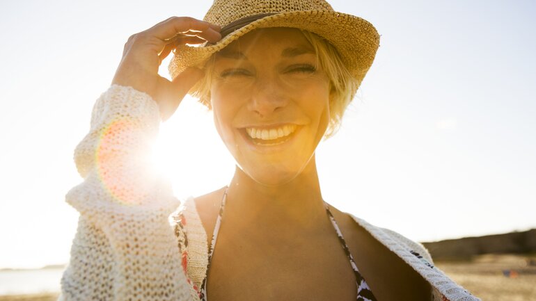 Frau mit Sonnenhut lächelt glücklich in die Kamera