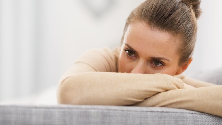 Frau sitzt traurig auf Sofa/Couch