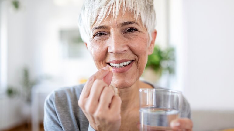 Frau in den Wechseljahren nimmt Tablette mit Glas Wasser ein