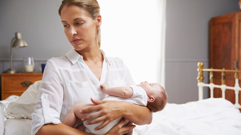 Frau mit Wochenbettdepression hält Baby auf dem Arm